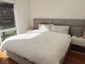 Un dormitorio con una cama grande, una mesita de noche, un ventanal y vistas al exterior.