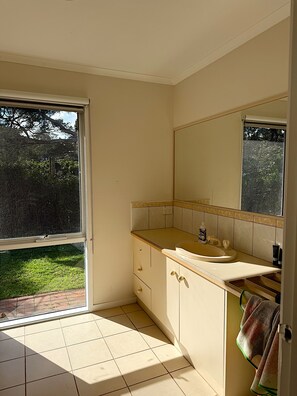Un baño con lavamanos, espejo y vista a un jardín por una ventana.