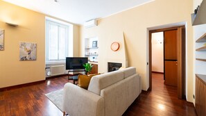 A living room with a sofa, a television, a fireplace, and a dining area visible through an open door. - [Isola - Porta Nuova] Elegant 1BDR with Balcony (Milano)