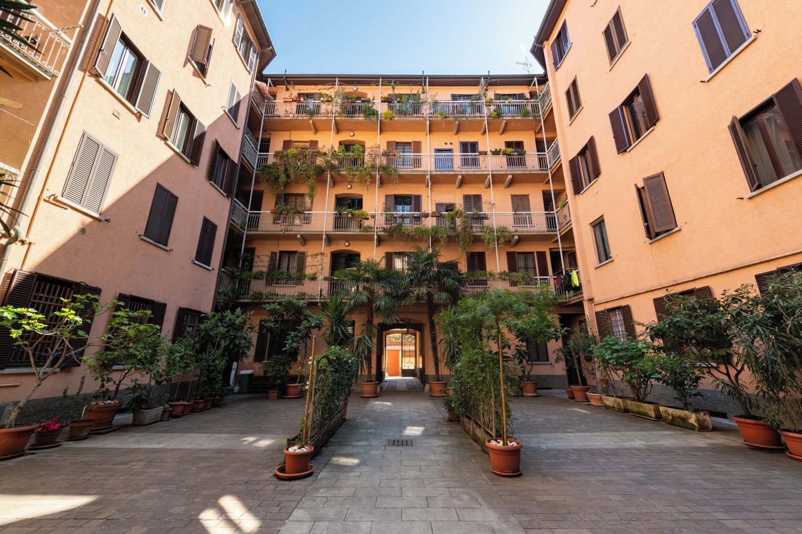 A courtyard with potted plants, a central entrance, and multi-story buildings with balconies.