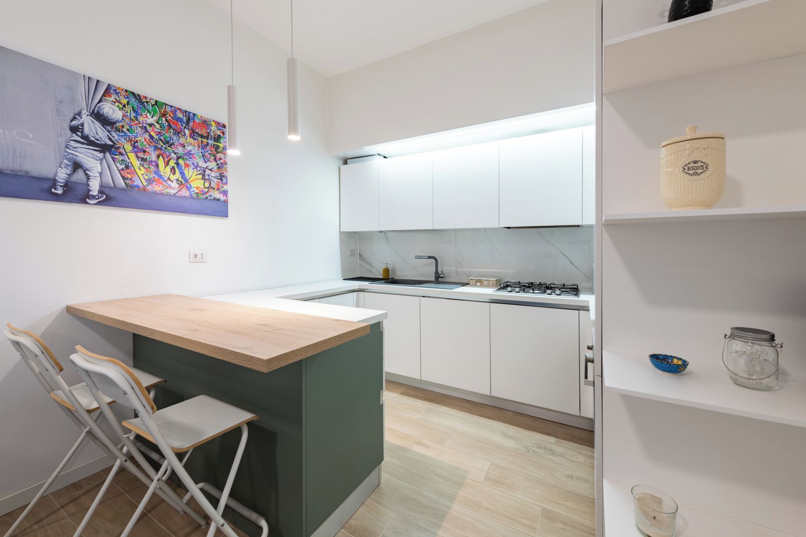A modern kitchen with white cabinets, a wooden island, and a colorful graffiti artwork on the wall.