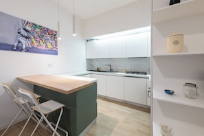 A modern kitchen with white cabinets, a wooden island, and a colorful graffiti artwork on the wall. - [Metro M1] Quiet & Modern Apt near Center (Milano)