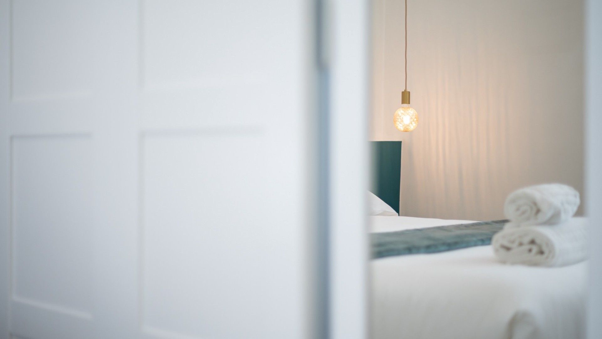 Ein Hotelzimmer mit einem Bett, einer Hängelampe und aufgerollten Handtüchern.