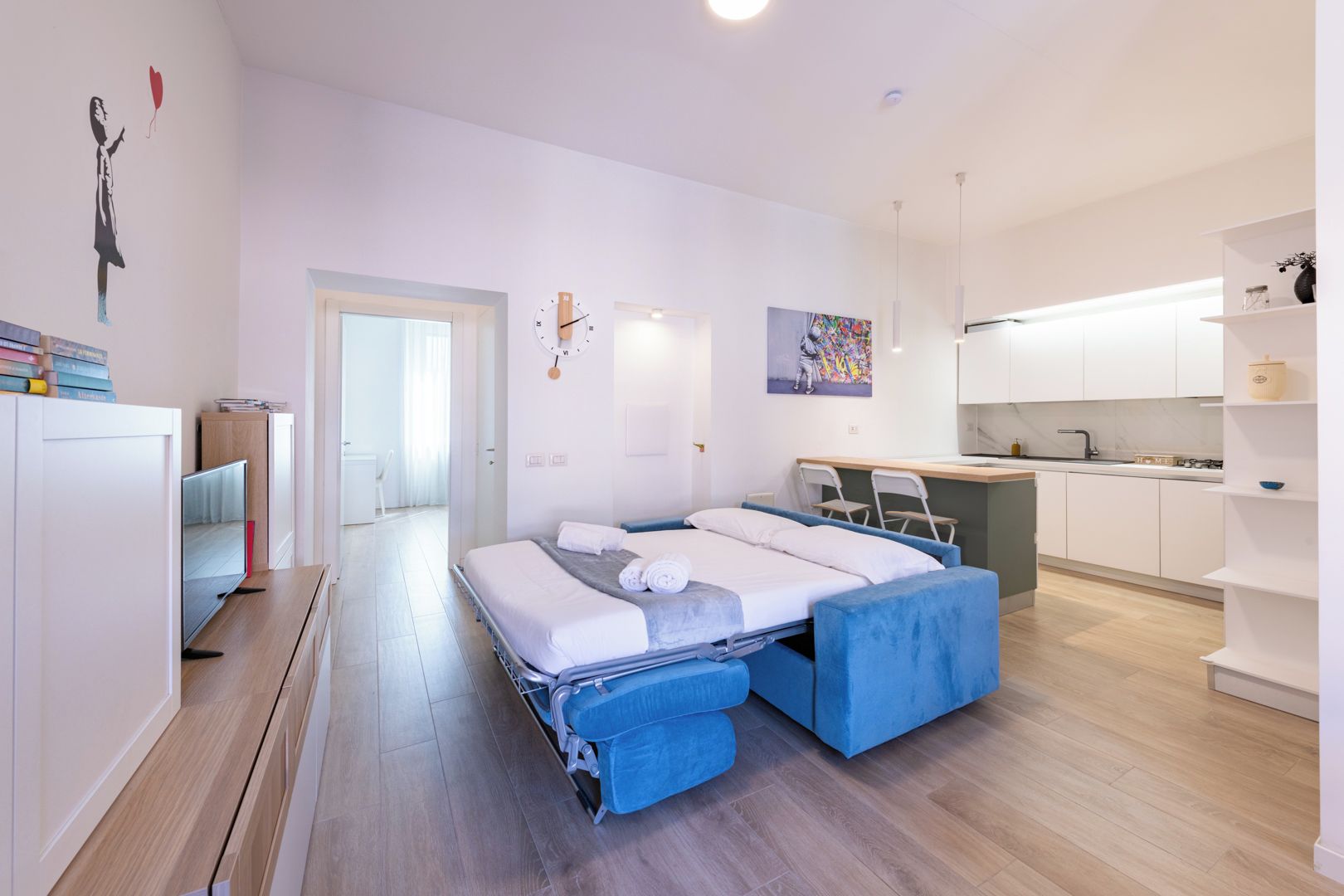 A modern hotel room with a bed, a desk, a kitchenette, and a bathroom.