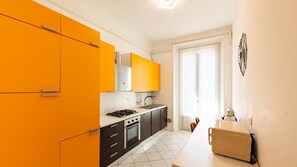 Eine kleine Küche mit modernen Geräten, einem weißen Fliesenboden und einer Tür zum Balkon.