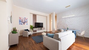 Ein modernes Wohnzimmer mit einer Couch, einem Fernseher und einem Essbereich mit Tisch und Stühlen.
