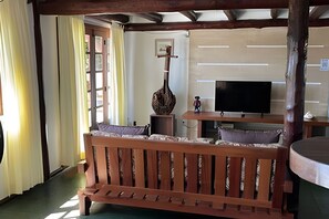 Eine hölzerne Bank mit Kissen, ein Fernseher auf einem Schrank und ein hölzernes Kreuz an der Wand.