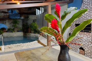 A modern outdoor area with a pool, a brick wall, and a potted plant with red flowers. - Casa 2 Porto Seguro 4 Quartos 2 Piscina (Porto Seguro)