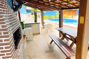 Eine Terrasse mit einer Ziegelwand, einer hölzernen Bank, einem Tisch und einem Pool im Hintergrund.