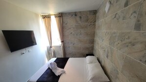 Une chambre d’hôtel avec un lit, un téléviseur à écran plat fixé au mur et une fenêtre avec des rideaux.