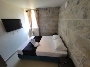 Quarto de hotel com cama, televisão de tela plana na parede e janela com cortinas.