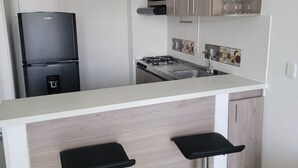 Une cuisine moderne équipée d’une cuisinière à gaz intégrée, d’un réfrigérateur noir et de deux tabourets de bar.