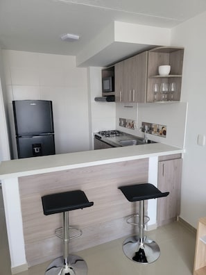 Uma cozinha moderna com fogão a gás embutido, geladeira preta e dois banquetas.