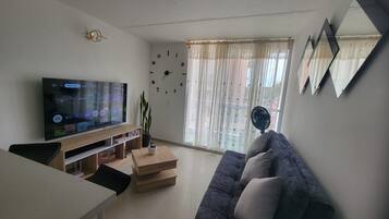 Una sala de estar con televisor de pantalla plana, sofá, mesa de centro y planta en maceta.
