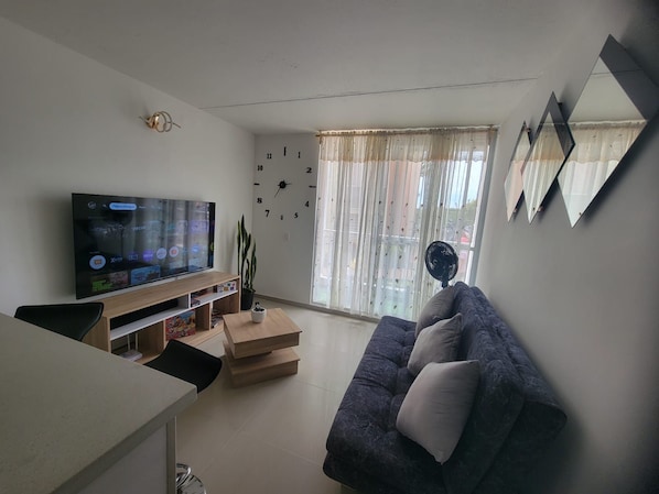 Uma sala de estar com televisão de tela plana, sofá, mesa de centro e planta em vaso.