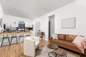 A modern living room with a brown sofa, a white armchair, and a dining area with a black table and wicker chairs. - 2-bedroom house in peaceful Indianapolis with cozy vibes (Indianapolis)