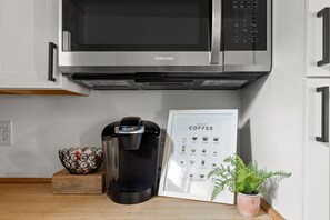 A kitchen with a coffee maker, a microwave, a coffee guide, a decorative bowl, and a potted plant. - 2-bedroom house in peaceful Indianapolis with cozy vibes (Indianapolis)