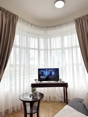 Ein Wohnzimmer mit einem Fernseher, der 'Die Grenze' auf Netflix zeigt, einem runden Holztisch mit einer Pflanze und einer Tasse, sowie einem Sofa mit einer weißen Decke.