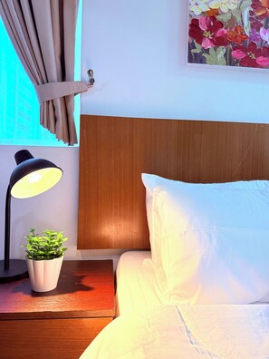 A hotel room with a wooden headboard, a bedside lamp, a potted plant, and a painting on the wall. - KLCC Studio | 10-Min Walk to Petronas Twin Towers (Kuala Lumpur)