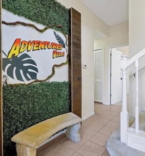 A hallway with a wall-mounted sign reading 'Adventures Villa,' a bench, and a staircase. - 4BR Townhouse- Near Disney (Kissimmee)