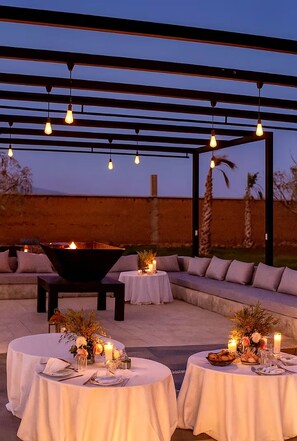 An outdoor dining area with round tables, candles, and a fire feature.