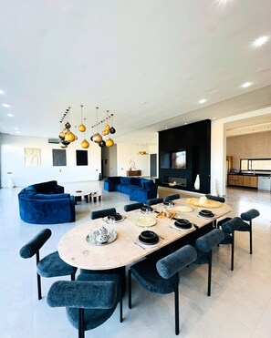 Ein modernes Wohnzimmer mit einem großen ovalen Esstisch, blauen Sofas und hängenden Pendelleuchten.