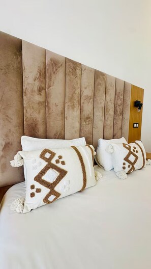 Ein Bett mit zwei Kissen mit geometrischen Mustern, einem Holz-Kopfbrett und einem an der Wand montierten Lichtschalter.