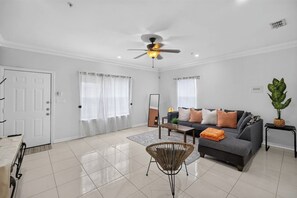 Uma sala de estar moderna com um sofá cinza, uma mesa de centro, um abajur e um ventilador de teto.