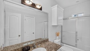 A bathroom with a granite countertop sink, a mirror, a toilet, a shower, and a cabinet. - Terracotta Central Spacious 2Bed/2bath Comfy Calm (McAllen)