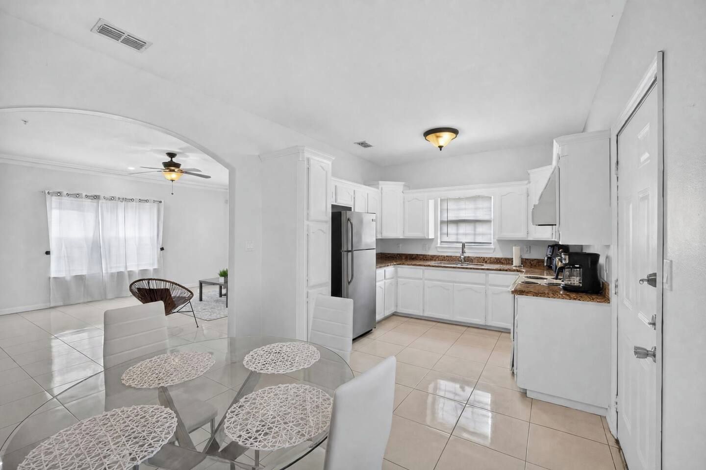 Una cucina moderna con mobili bianchi, una zona pranzo con tavolo e sedie in vetro e una ventola a soffitto.