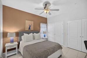 Quarto com cama, mesas de cabeceira, ventoinha no teto e guarda-roupa.