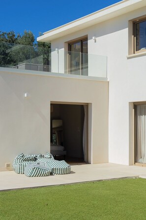 Ein modernes, zweistöckiges Haus mit Balkon, Glastür und einem Rasenstück.