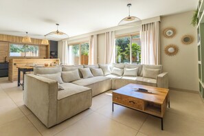 Ein modernes Wohnzimmer mit einer Eckcouch, einem Holztisch und einem Essbereich, im Hintergrund eine Küche.