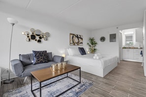 A modern living room with a sofa, coffee table, and a bed with a bedside table. - Cozy Nook Studio 8 min to Disney & Universal | Orl (Kissimmee)