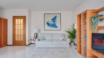 A living room with a sofa, a television, a door, and a wall-mounted picture.