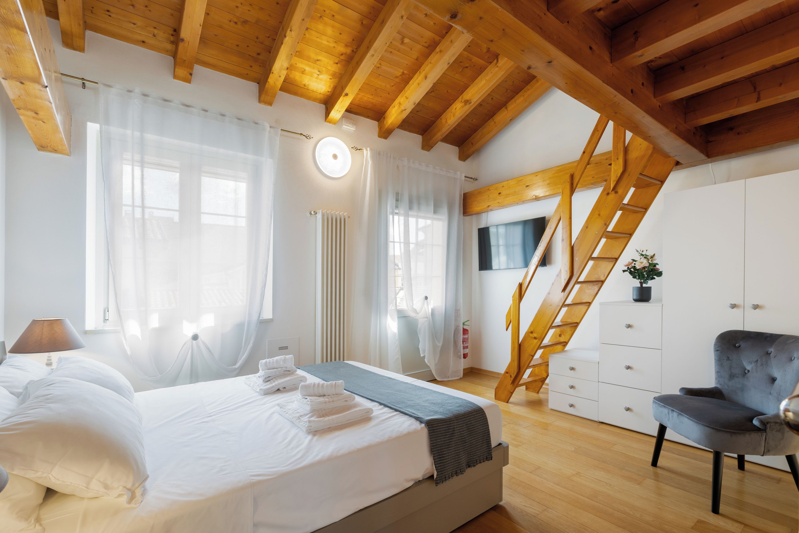 Une chambre à coucher avec un lit, une chaise, une commode, un radiateur et une fenêtre avec des rideaux.