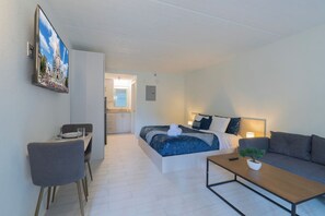 A modern hotel room with a bed, a sofa, a desk, and a dining area. - Breezy Studio 8 min to Disney + Parking | Orl (Kissimmee)