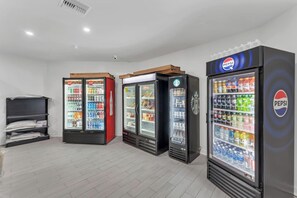 Een rij drankautomaten met Pepsi en Coca-Cola branding, een zwarte koelkast en een plank met flessen water.