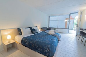 Een hotelkamer met een bed, nachtkastje en uitzicht op zee door een groot raam.