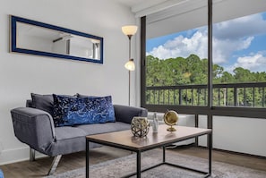 A modern living room with a grey sofa, a blue patterned pillow, a wooden coffee table, a globe, and a floor lamp. - Studio Escape 7 min to Disney World +Parking | Orl (Kissimmee)