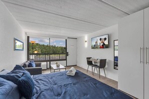 A modern room with a bed, a desk, and a balcony with a view of greenery. - Studio Escape 7 min to Disney World +Parking | Orl (Kissimmee)