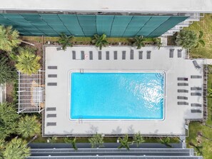 An aerial view of a swimming pool with adjacent lounge chairs and a fenced area with palm trees. - Studio Escape 7 min to Disney World +Parking | Orl (Kissimmee)