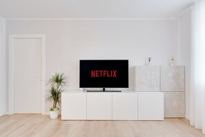 Un soggiorno moderno con un mobile TV bianco, una TV a schermo piatto che mostra 'NETFLIX' e una piccola pianta in vaso.