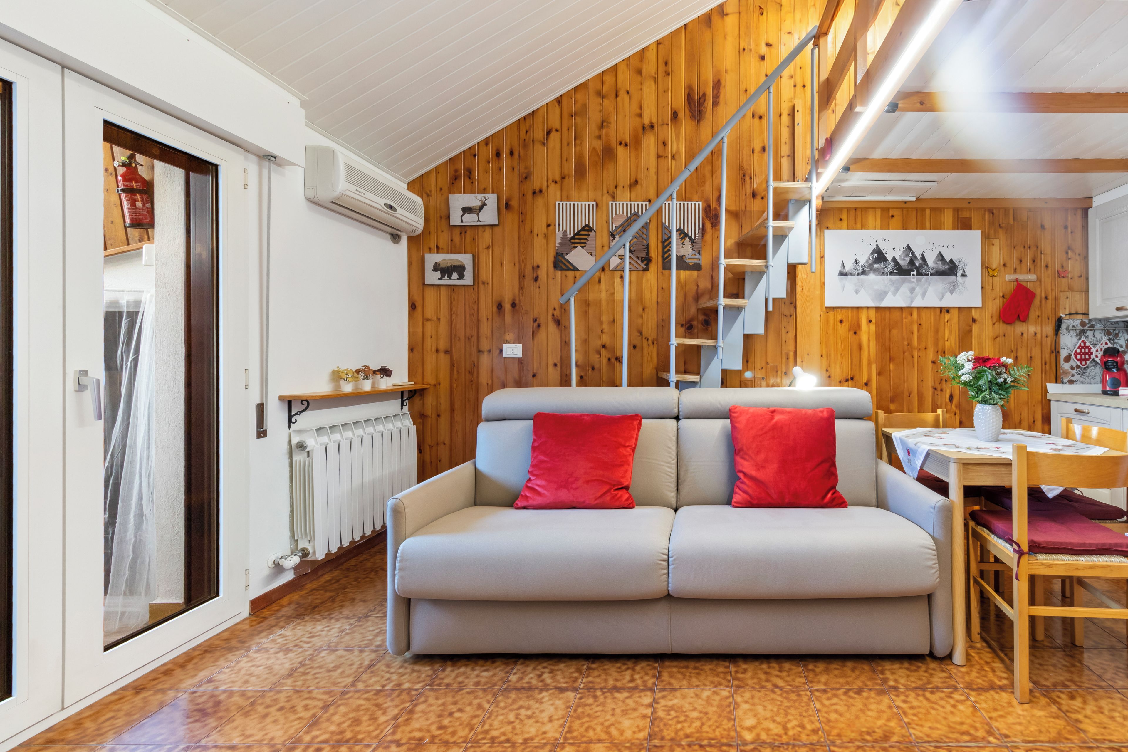 A cozy living room with a wooden wall, a sofa, a dining table, and a staircase.