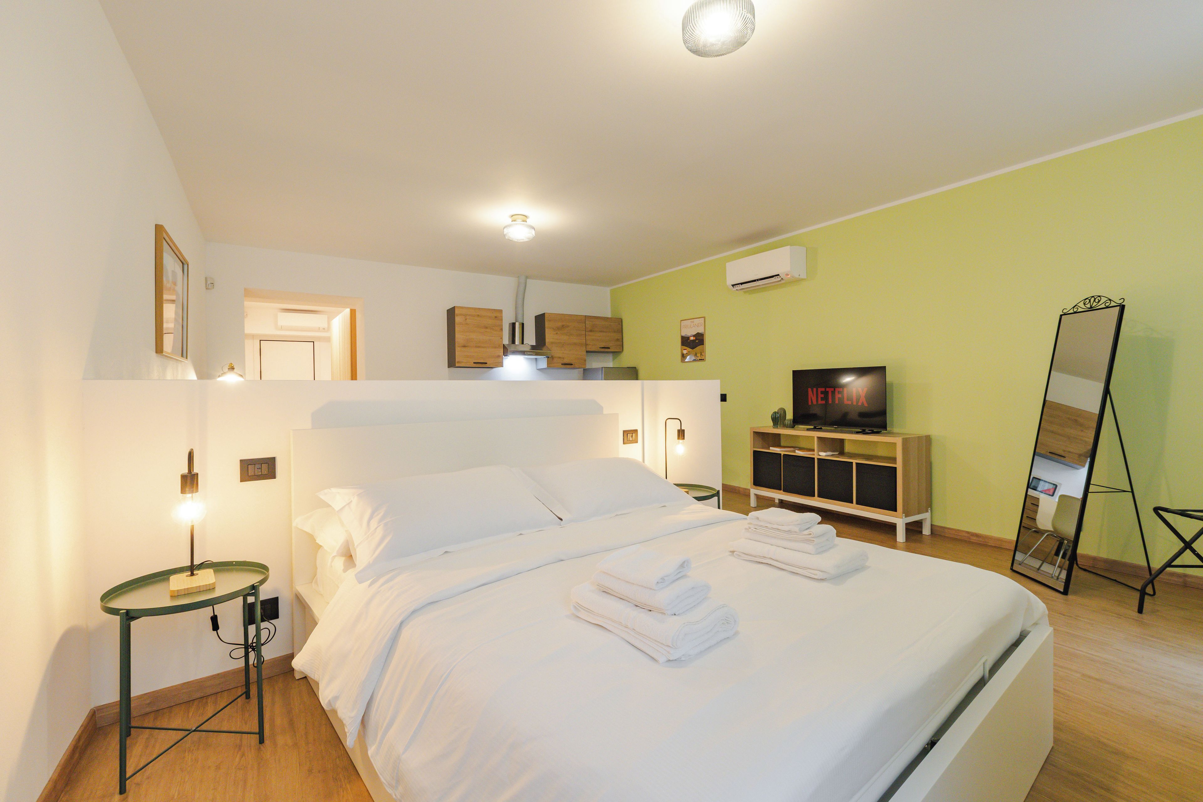 Une chambre d’hôtel avec un lit, une télévision, un miroir et une petite table avec une lampe.