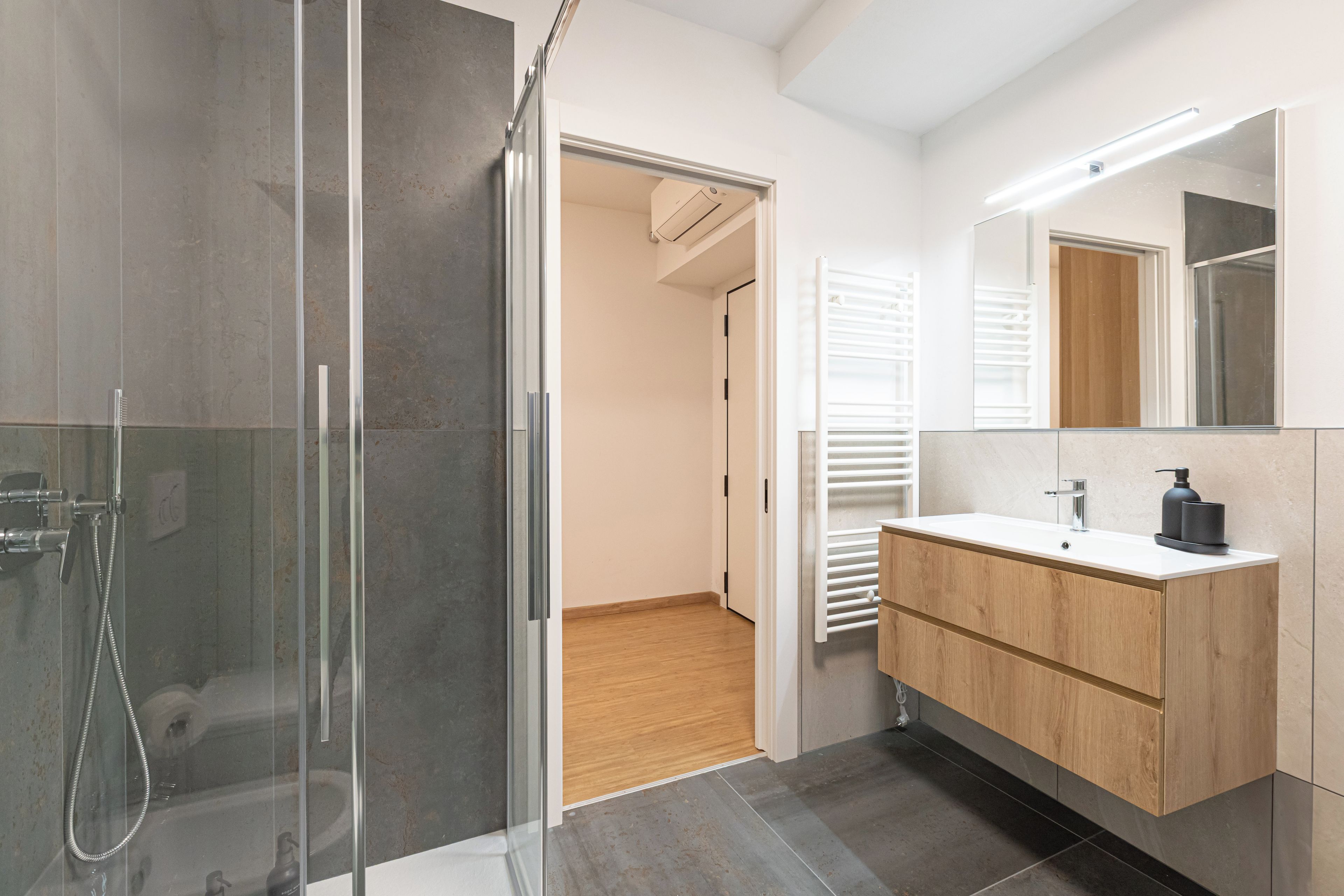 A modern bathroom with a glass shower enclosure, a wooden vanity, and a large mirror.