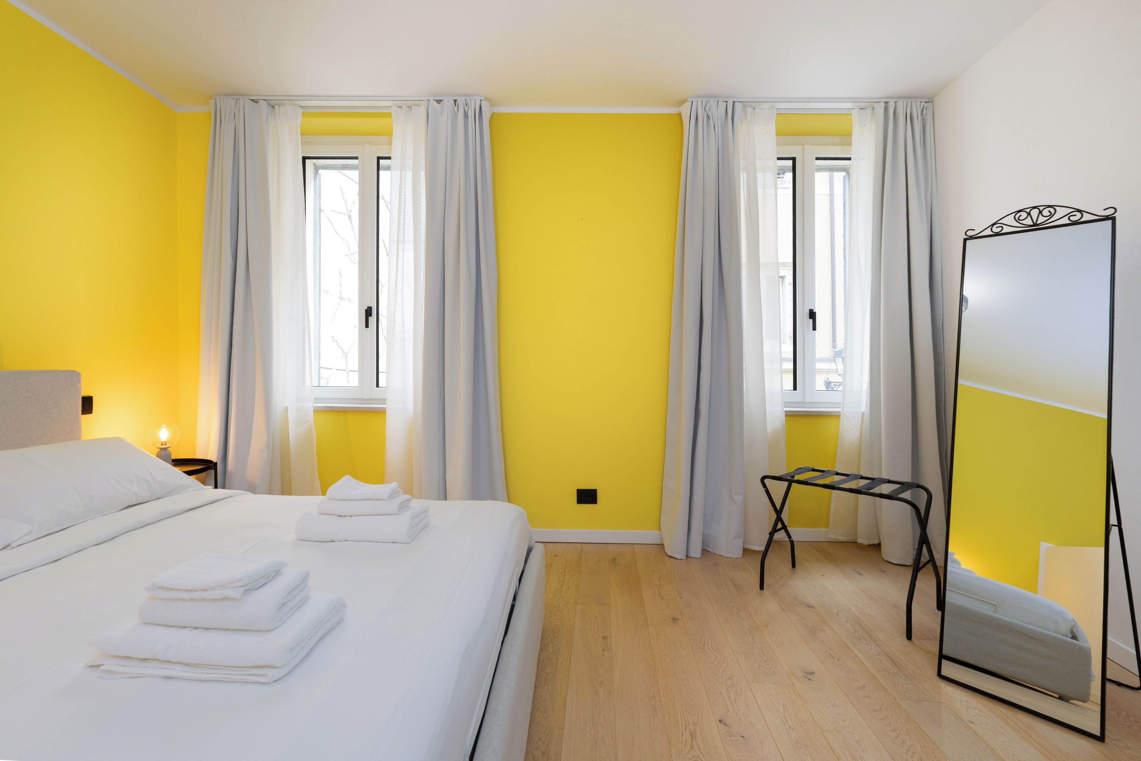 A hotel room with a bed, a mirror, and a window with curtains.