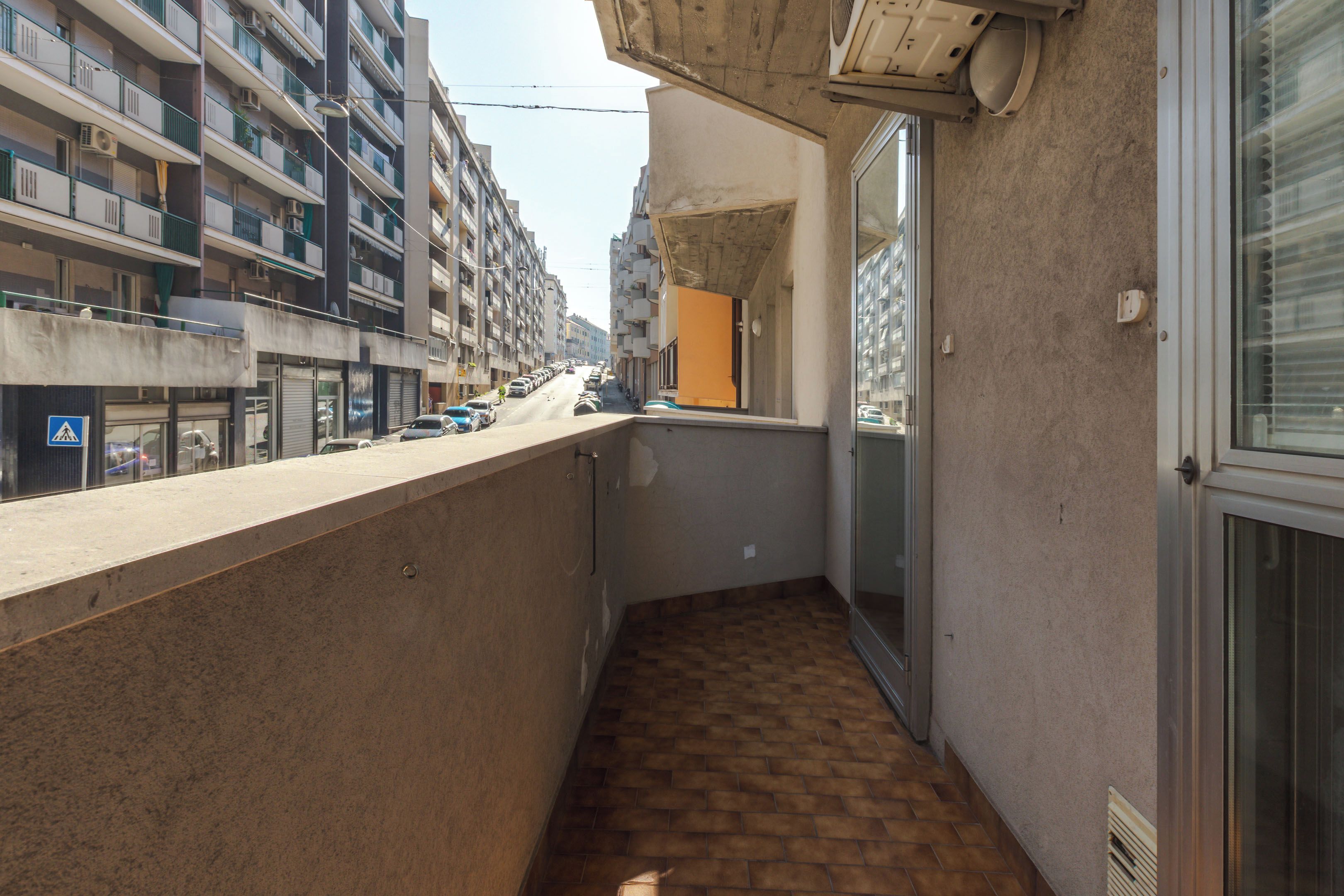 En smal balkong med ett kaklat golv, utsikt över gatan och en byggnad med flera balkonger.