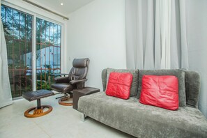 Ein modernes Wohnzimmer mit einem grauen Sofa, roten Kissen, einem braunen Ledersessel und einem kleinen Holztisch.