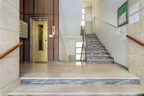 Un escalier en marbre, doté d’une rampe, mène à un ascenseur dont la porte est dorée.